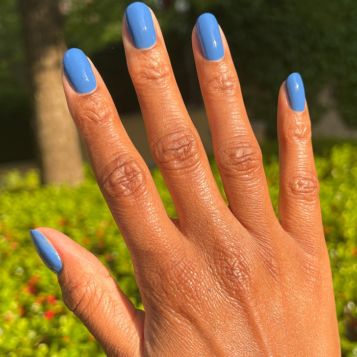 Hand with medium-length nails painted in Blue Canoe gel polish by Olive and June outdoors in natural light