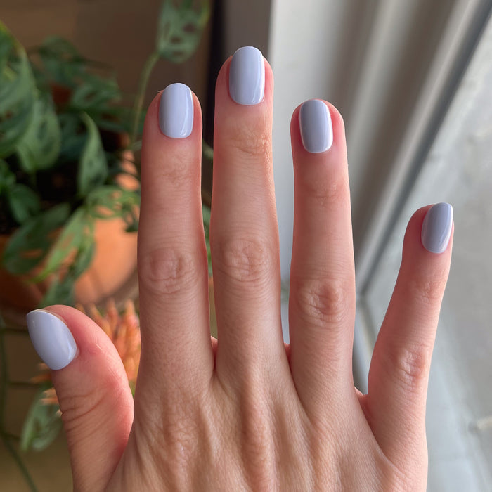 BP - Press-On | Extra Short | Round showing hand with icy light blue extra short round false nails indoors by window light