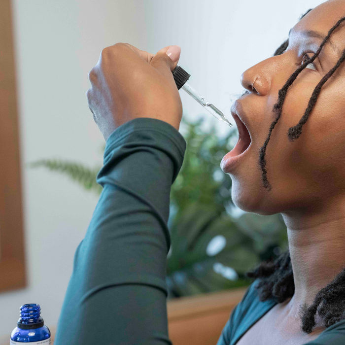 Close-up of a person tipping a dropper into their open mouth to take Heartburn support drops in a home setting