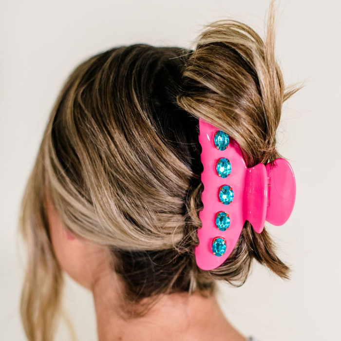 Pink hair clip with blue gems in a person's hair against a white background
