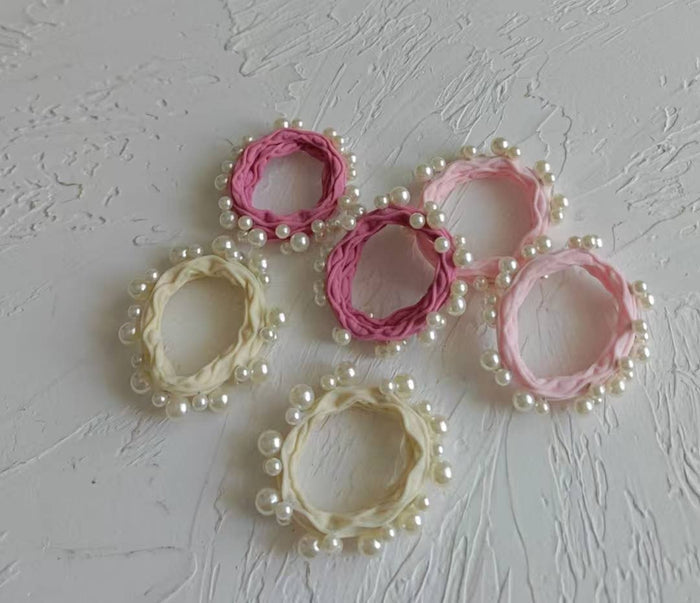 Set of pink and beige hair ties with pearl embellishments on a textured gray background