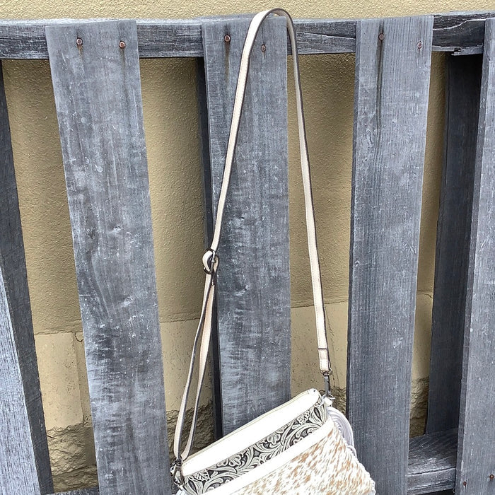 This cowhide and tooled leather crossbody bag features fringe sides and zips closed. The strap is removable and adjustable. View of crossbody strap.