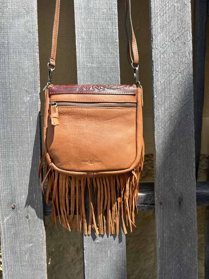 This Brown leather crossbody bag features fringe sides and a tooled flap with a whipstitch border. It has a removable and adjustable shoulder strap. Rear view showing pocket that zips closed.