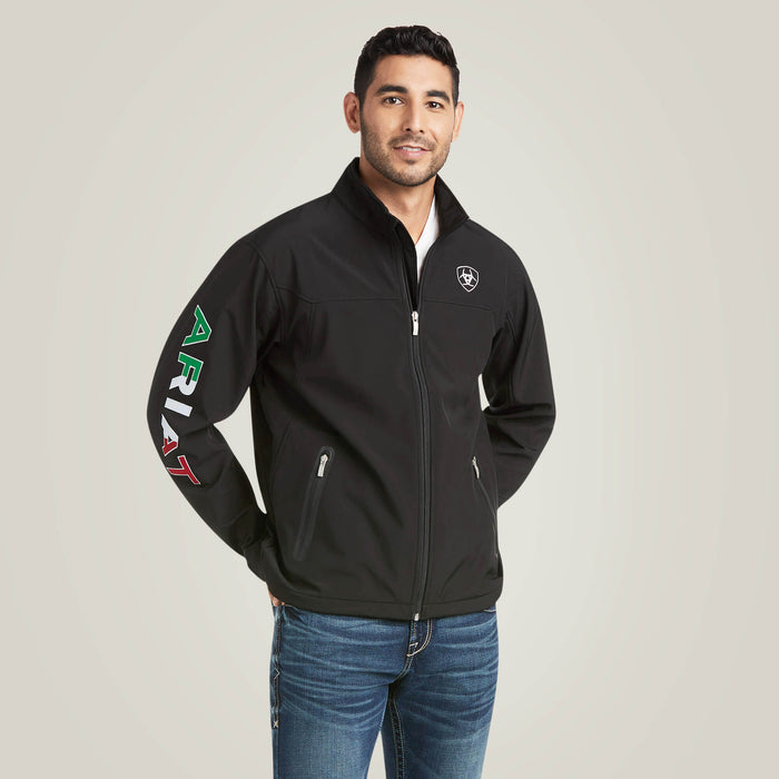 Men's Ariat softshell Team logo jacket in black with a blocked Ariat logo in white, green, and red representing the Mexican Flag. Front view showing jacket zipped up and both front pockets zipped closed.
