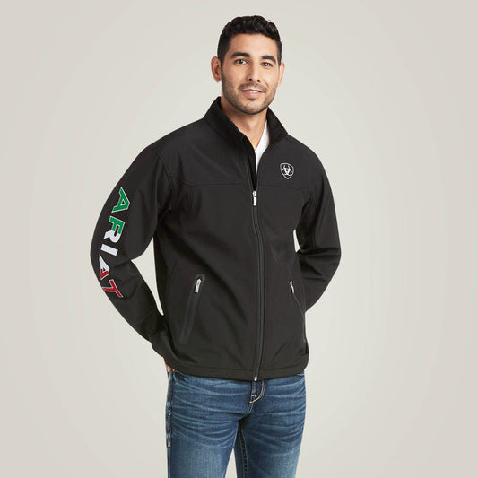 Men's Ariat softshell Team logo jacket in black with a blocked Ariat logo in white, green, and red representing the Mexican Flag. Front view showing jacket zipped up and both front pockets zipped closed.