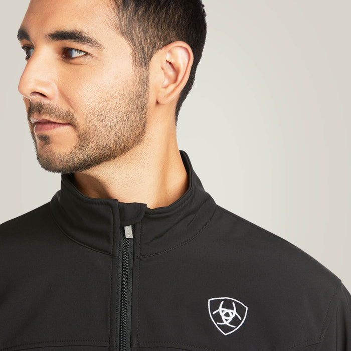 Men's Ariat softshell Team logo jacket in black with a blocked Ariat logo in white, green, and red representing the Mexican Flag. Close up of front collar and Ariat shield logo on left chest.