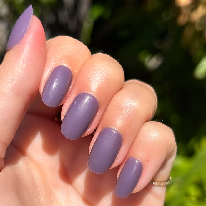 Art Class - Press-On | Short | Round showing hand with muted eggplant purple short round press-on manicure in sunlight outdoors