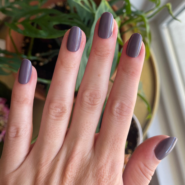 Art Class - Press-On | Short | Round showing hand with smooth muted eggplant purple short round press-on manicure by a window in natural light