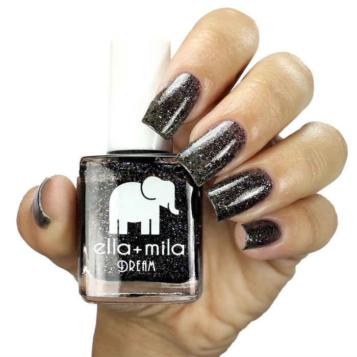 Black Magic black tinted glitter nail polish on a medium skin tone, holding the bottle