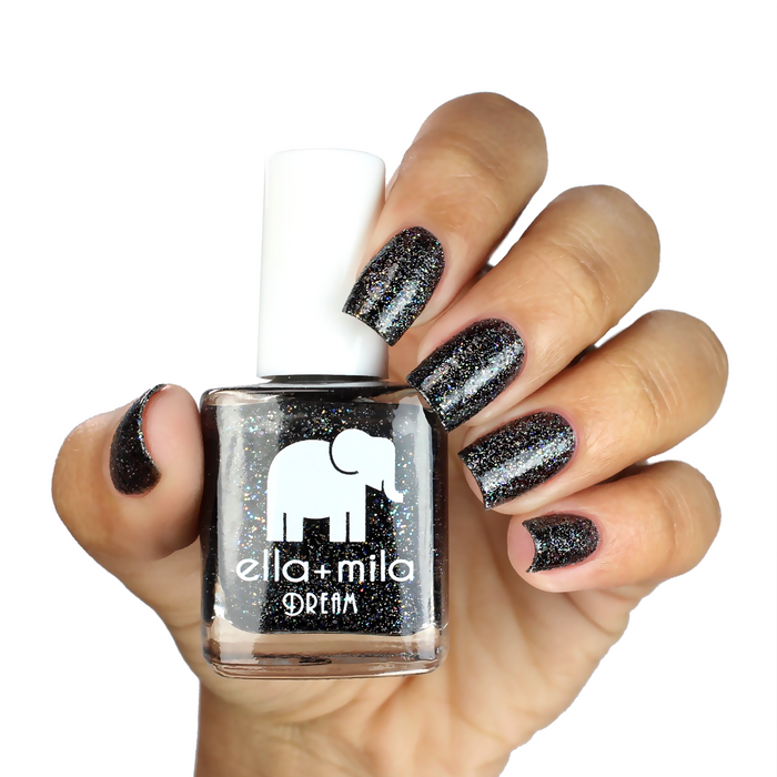 Black Magic black glitter nail polish on a medium-deep skin tone, hand holding the bottle