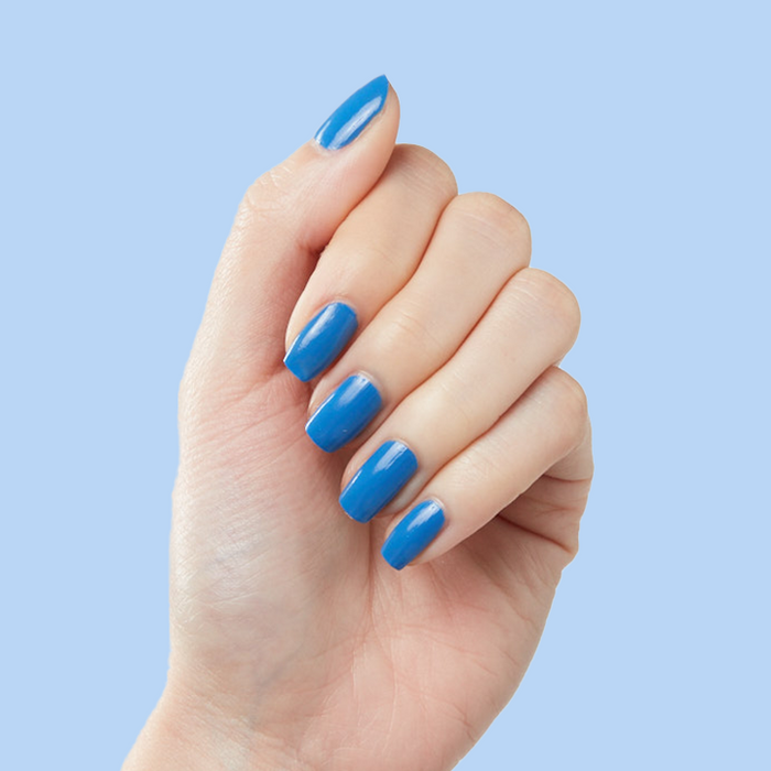Hand with medium nails painted in Blue Canoe long-lasting polish by Olive and June against light blue background