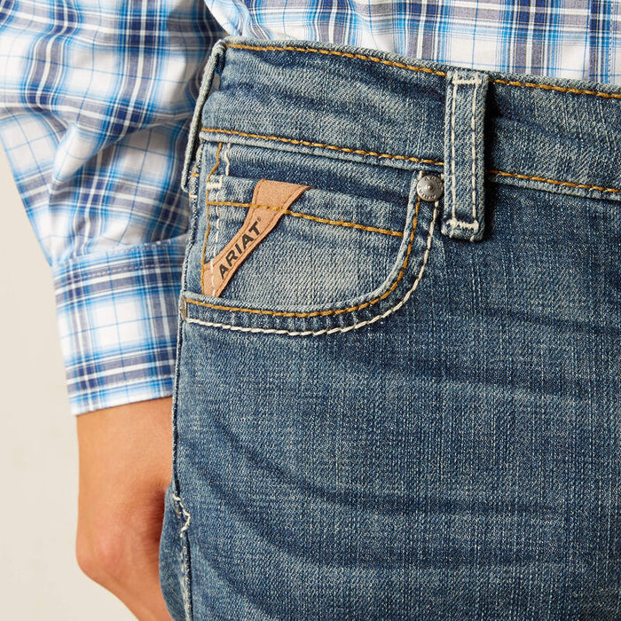 Boy's Ariat relaxed fit boot cut jeans in a medium wash. Close up of front pocket showing Ariat logo tag.