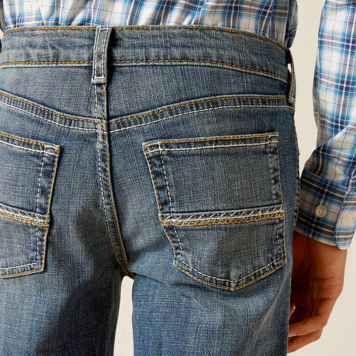 Boy's Ariat relaxed fit boot cut jeans in a medium wash. Rear view showing stitching on pockets.