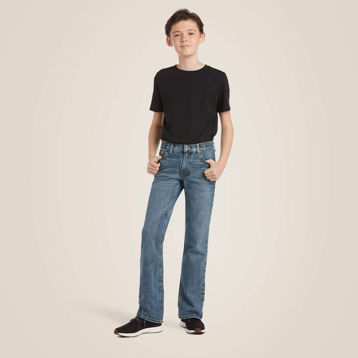Boy's Ariat M5 slim straight jeans, in a medium wash. Full front view on model with shirt tucked.