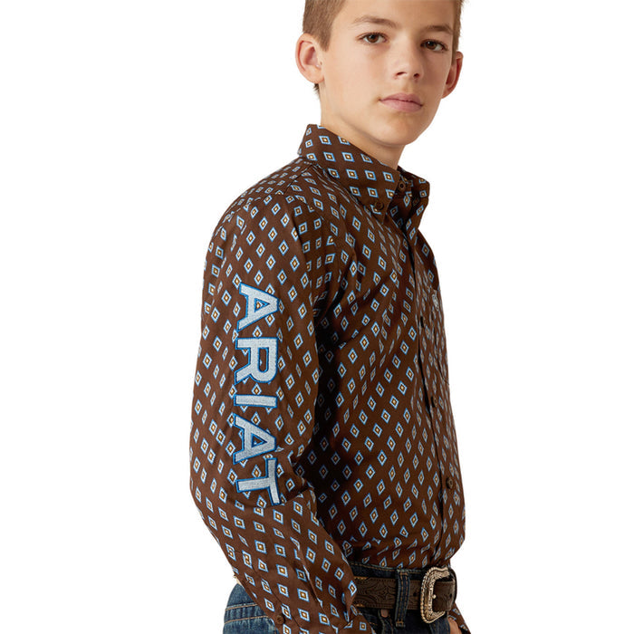 Boy's Ariat long sleeve team logo shirt in brown with a blue diamond pattern. Side view of bold Ariat team logo on left sleeve.