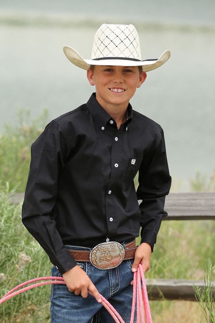A boy wearing a black long sleeve button down shirt with an embroidered logo on the pocket.