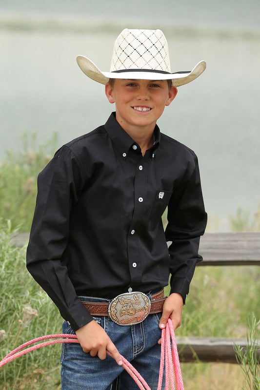 A boy wearing a black long sleeve button down shirt with an embroidered logo on the pocket.