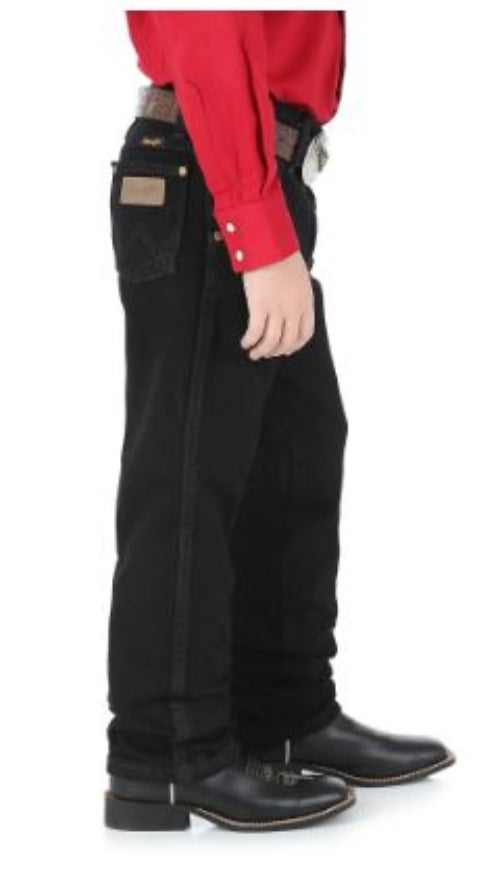 Sideview of a boy wearing overdyed black Wrangler cowboy cut jeans with a five-pocket design and flat copper rivets.