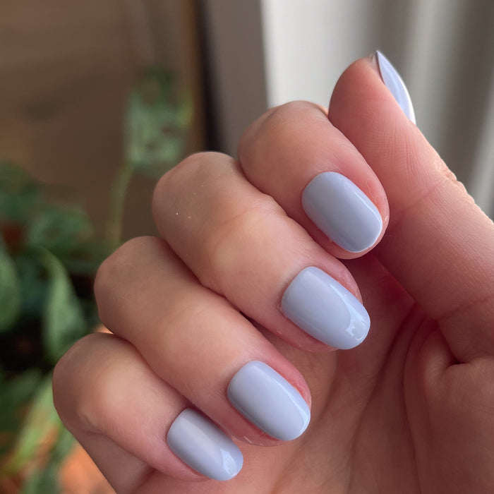 BP - Press-On | Extra Short | Round showing hand with icy light blue extra short round press-on false nails indoors by plants