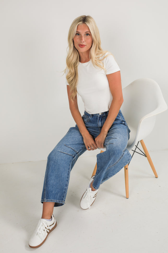 Woman sitting on a white chair wearing a white t-shirt and blue jeans.