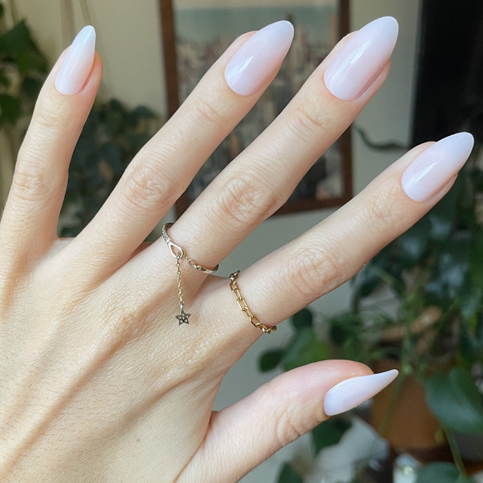 CCT - Press-On | Long | Almond showing hand with sheer soft pink long almond press-on manicure indoors with decorative rings