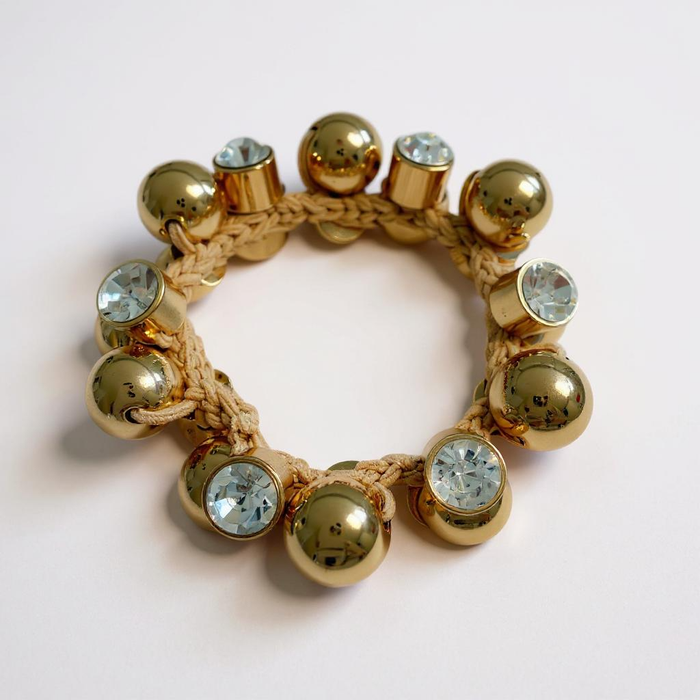 Bracelet with gold beads and crystal-like stones on a light pink background