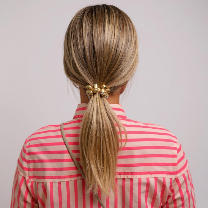 Person with blonde hair in a ponytail wearing a pink and red striped shirt on a plain background