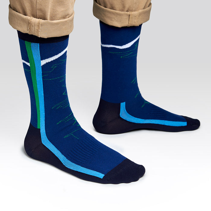 A person wearing cuffed khaki pants and blue socks with green, blue, and white geometric patterns stands on a light gray background.