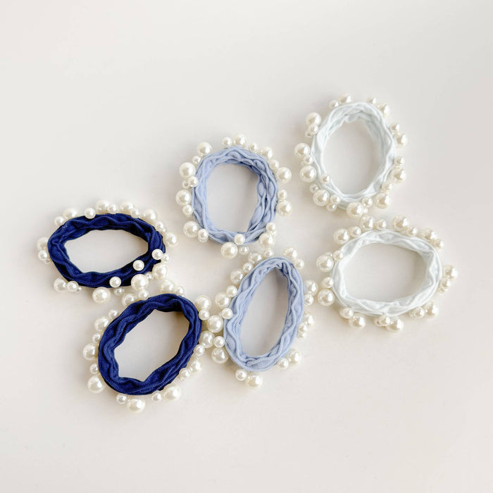 Set of pearl-embellished hair scrunchies in blue and white on a light background