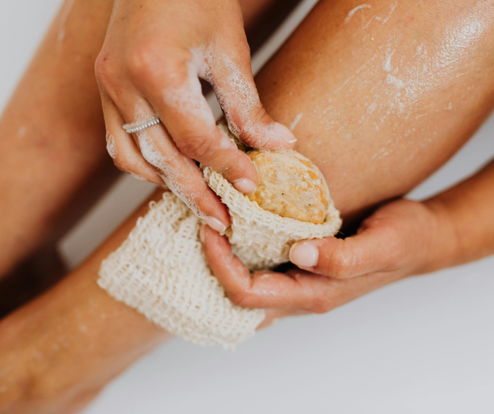 Person scrubbing their leg with a sisal soap bag with a natural bar of soap inside