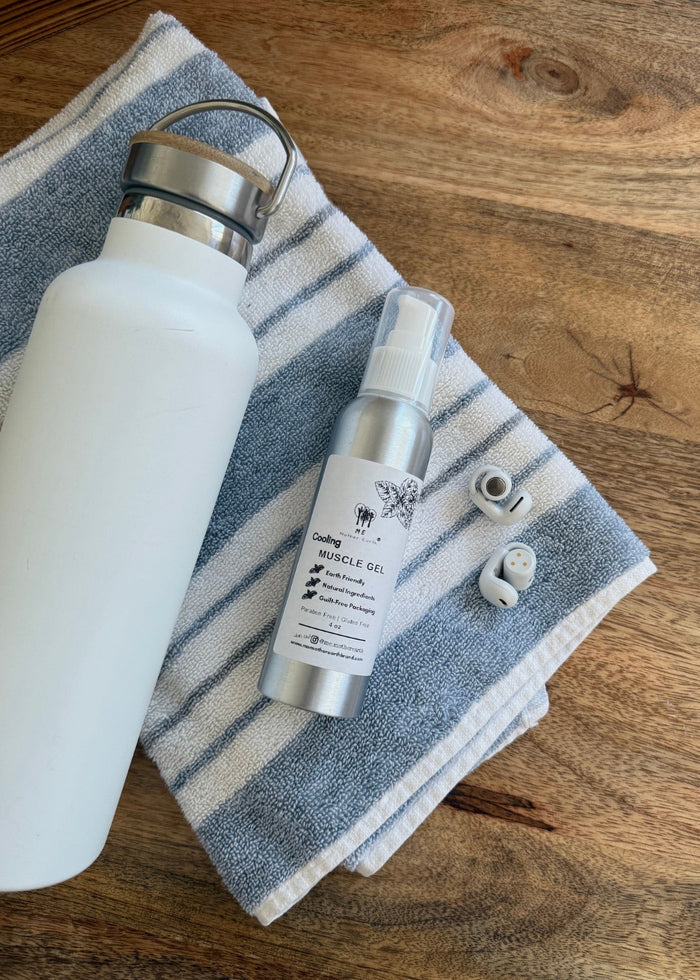 White water bottle, small bottle of muscle gel, and earbuds on a striped towel on a wooden surface
