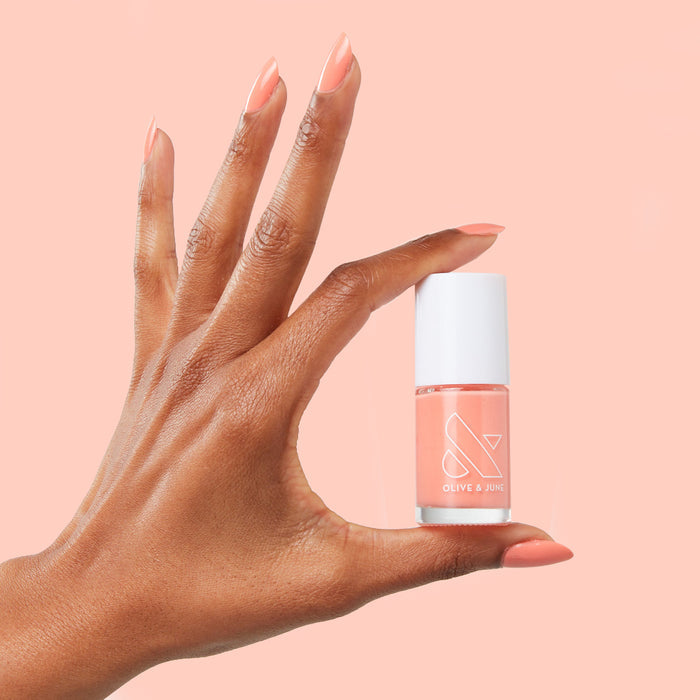 Hand with nails painted in bright cantaloupe Counselor In Training gel polish by Olive and June holding polish bottle
