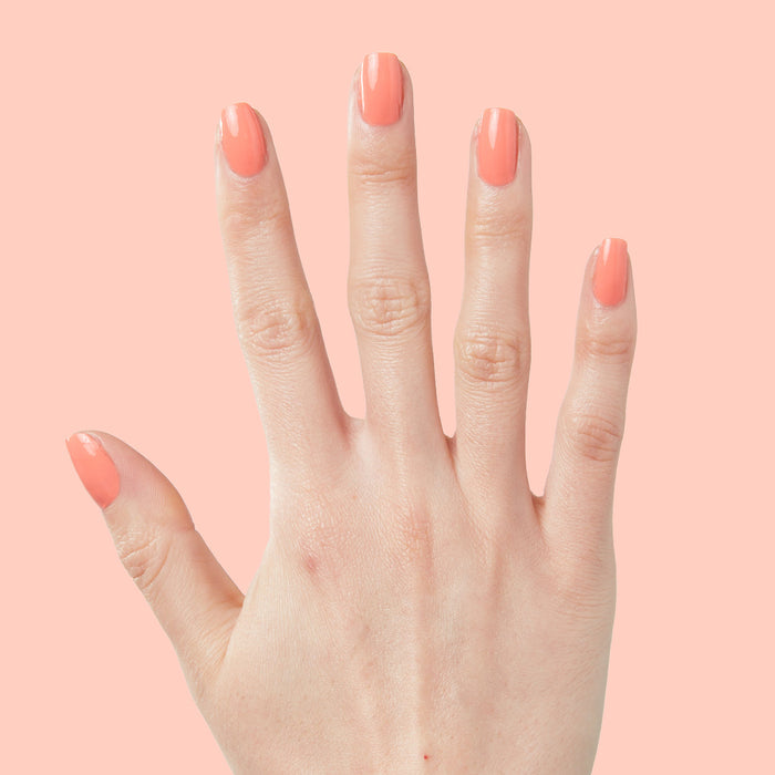 Hand with nails painted in bright cantaloupe orange Counselor In Training gel polish on pale peach background