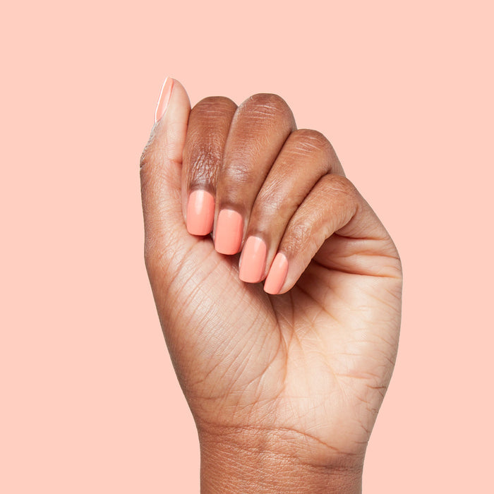 Close-up of hand with nails painted in bright cantaloupe orange Counselor In Training gel polish on matching background