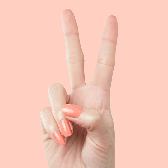 Hand with nails painted in cantaloupe orange Counselor In Training gel polish on soft peach background