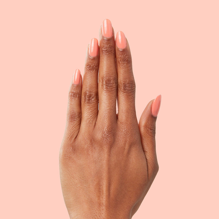 Hand with nails painted in cantaloupe orange Counselor In Training gel polish against soft peach background for manicure