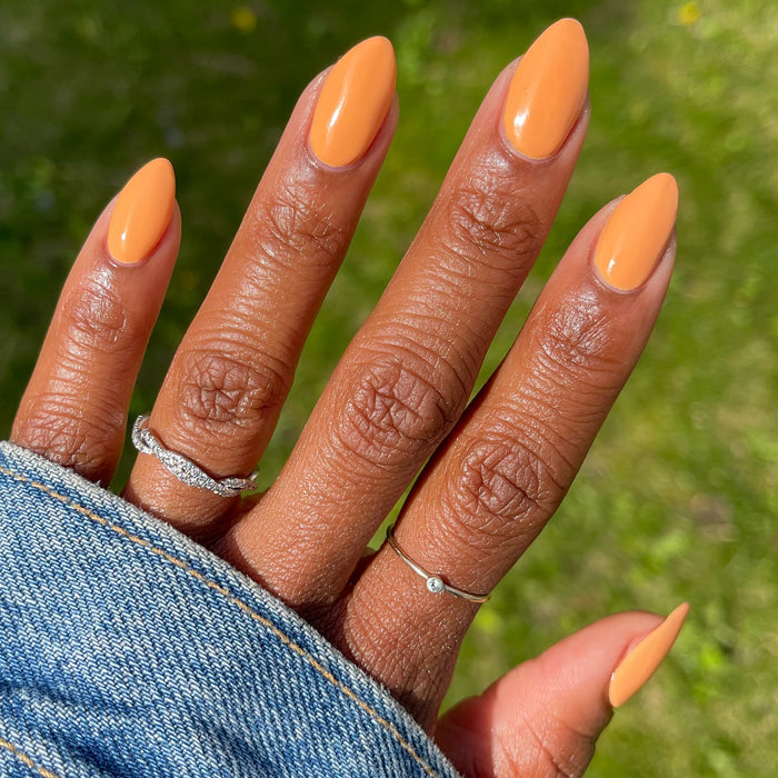 Hand with almond-shaped nails polished in Counselor In Training gel polish by Olive and June outdoors on grass
