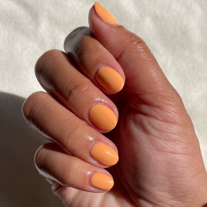 Fingers with nails coated in Counselor In Training gel polish showing a smooth cantaloupe mani on natural skin tone