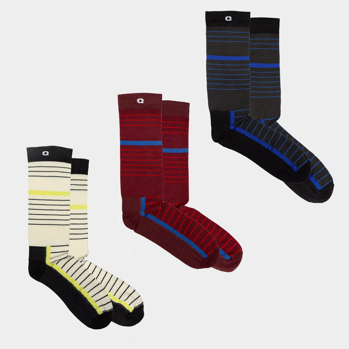 Three pairs of socks in different colors with horizontal stripes: one cream and black with yellow accents, one burgundy and red with gray, and one black and blue with gray toes and heels, arranged on a plain background.