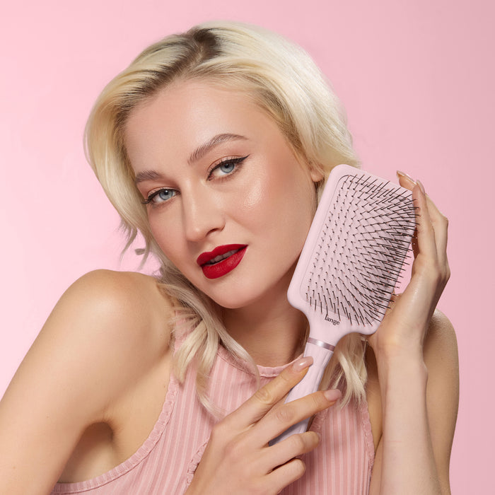 Model smiling while holding a blush detangling paddle brush