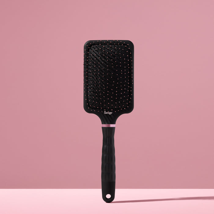 black L’ange detangling paddle brush with nylon bristles standing upright on pink background