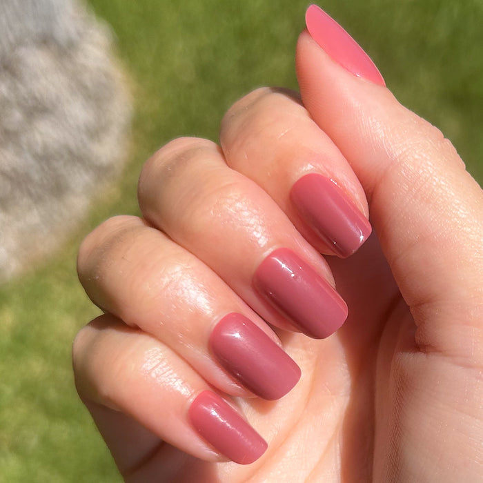 Fig Ranch - Press-On | Short | Squoval showing hand with short squoval cool-toned fig pink press-on manicure outdoors on grass background