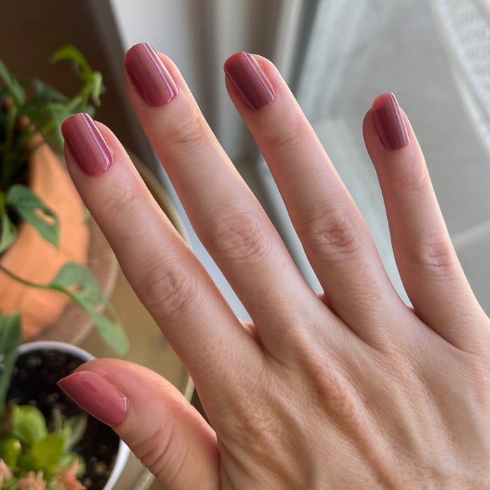 Fig Ranch - Press-On | Short | Squoval showing hand with short squoval cool fig pink press-on manicure indoors near natural light and plants