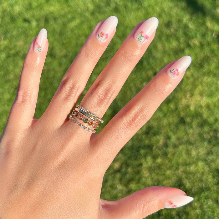 Floral Fields - Press-On | Medium | Oval showing medium oval false nails with delicate red floral designs on natural hand outdoors