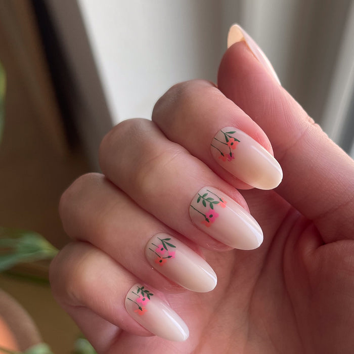 Floral Fields - Press-On | Medium | Oval showing natural medium oval nails with small red floral designs on hand near window light