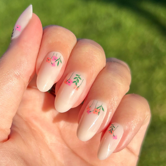 Floral Fields - Press-On | Medium | Oval showing medium oval press-on nails with delicate red floral designs on hand outdoors in sunlight