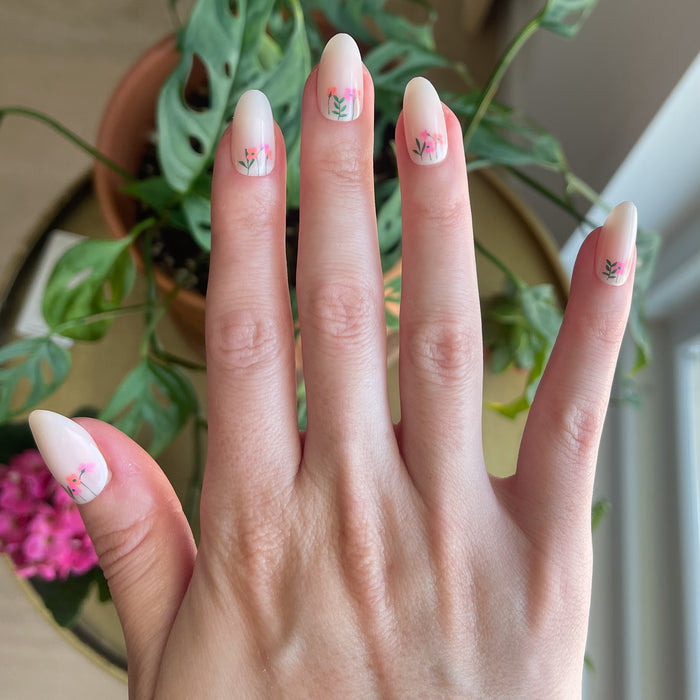 Floral Fields - Press-On | Medium | Oval showing medium oval press-on nails with delicate red floral designs on hand indoors near window light