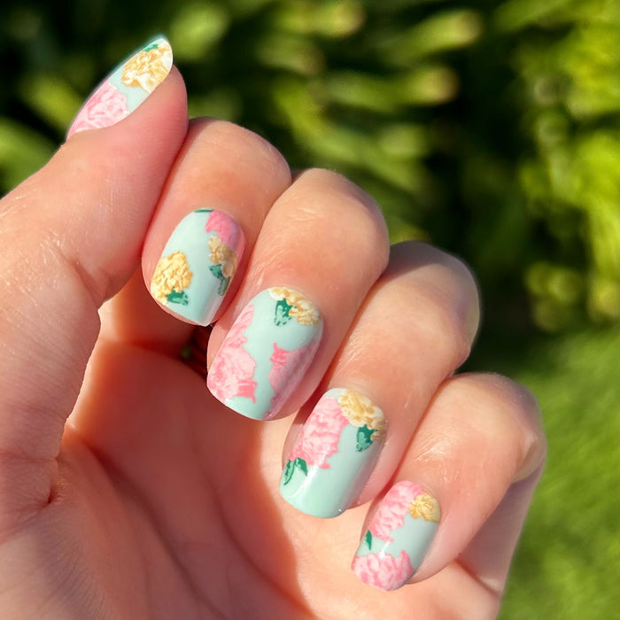 Full Floral - Press-On | Extra Short | Squoval showing pastel green squoval nails with pink and yellow floral designs on hand outdoors