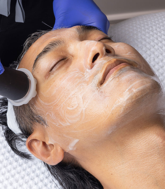 A person is receiving a facial treatment with a product applied to their face using a device.