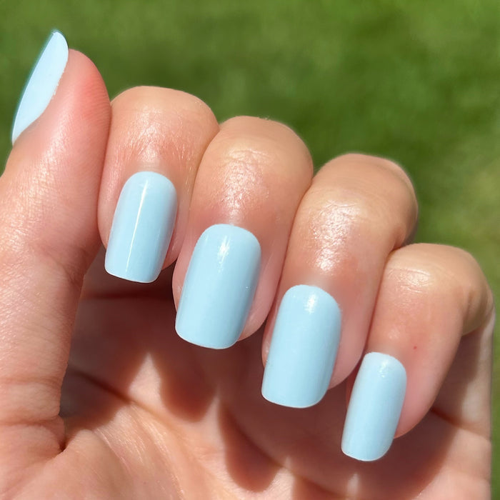 Honest & True - Press-On | Short | Squoval showing hand with serene blue short squoval press-on nails outdoors on green grass background